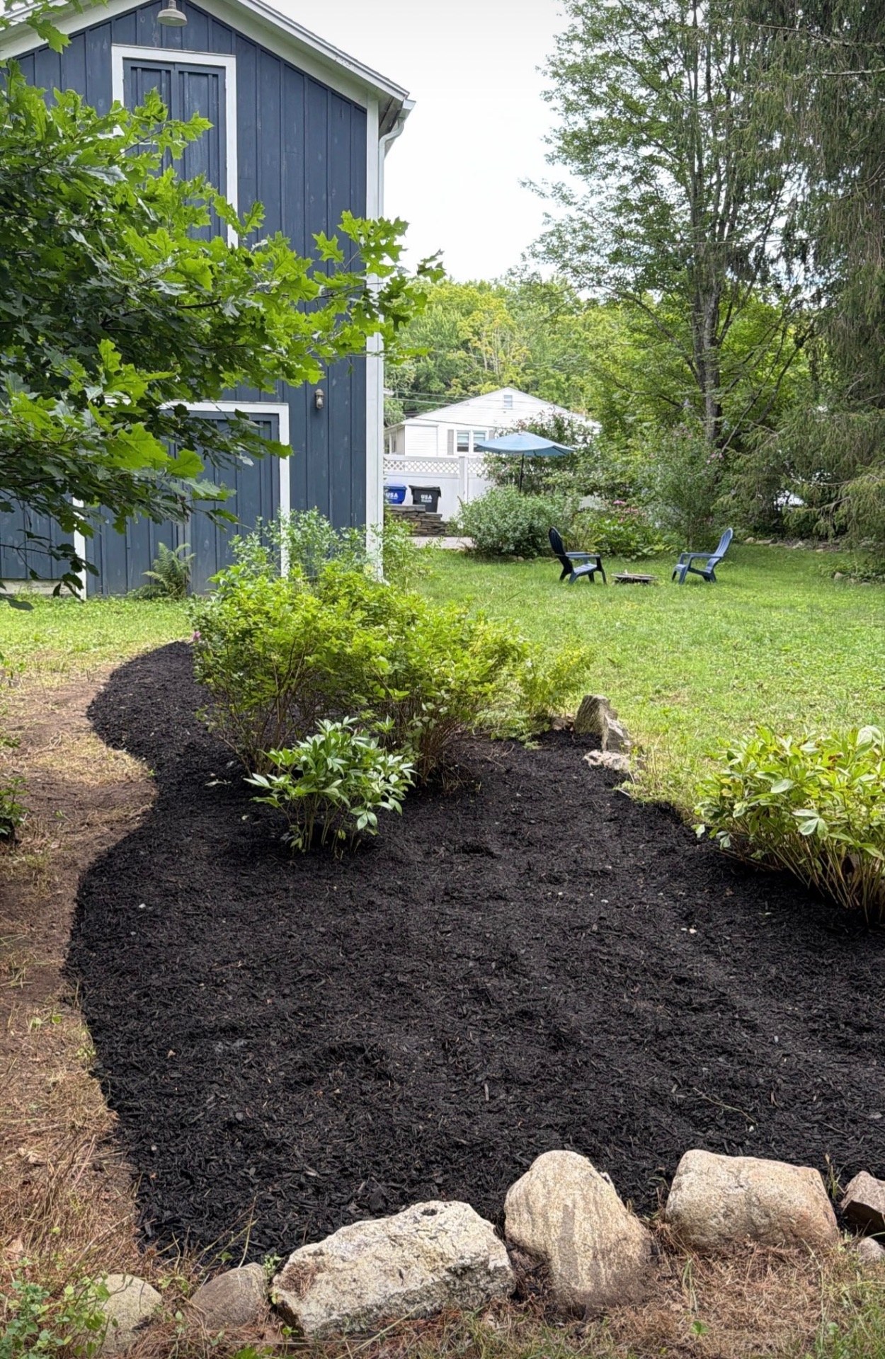 Curved Mulch Bed — Fresh black mulch with hand-set stone border and clean edging.
